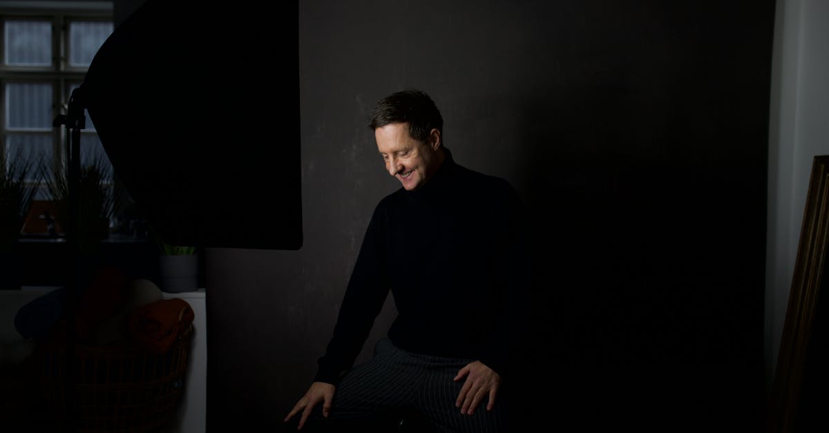 Man in black turtleneck in a dimly lit studio setting, smiling.