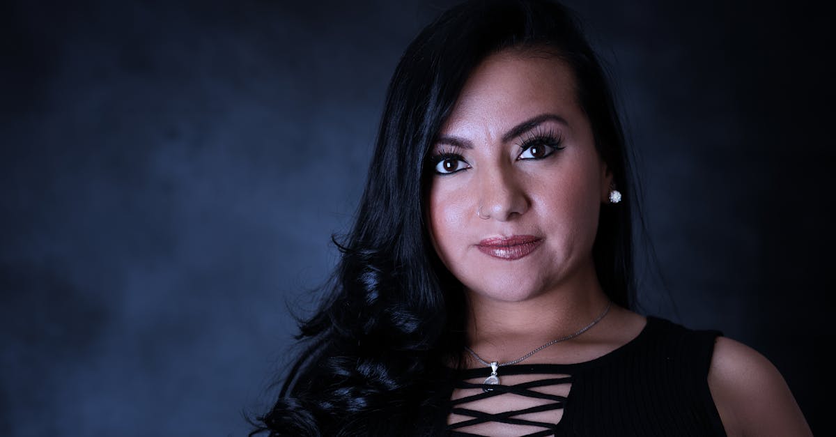 A sophisticated portrait of a woman with long dark hair and a confident expression against a black backdrop.