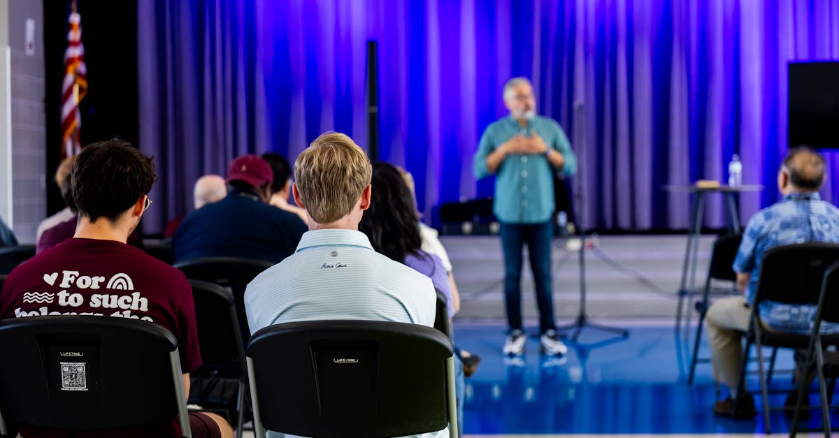 People listening to a speaker in a hall with blue lighting, exhibiting interest and engagement.